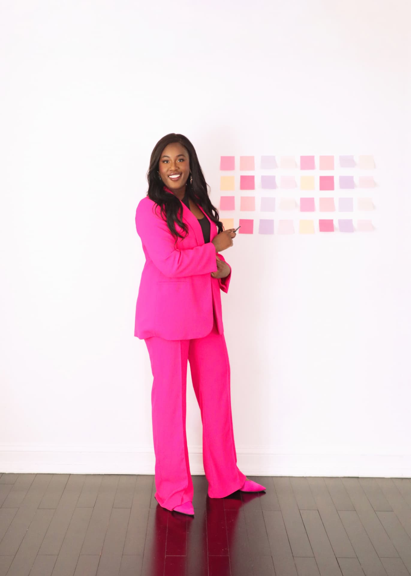 Shampaigne Graves in a hot pink suit standing beside a wall of pink and lavender sticky notes